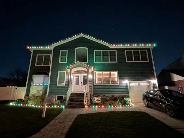 Raised ranch with dark green siding at night, red, green and white bulbs along the roofline and entry gable and matching lights along the front beds