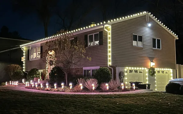 Split-level home with warm white bulbs along the roofline, corners and garage doors and lit stakes lining the front walk