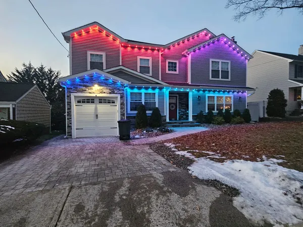 Two-story home at dusk with permanent roofline lights in red, pink, purple and blue over the garage, porch and upper gables