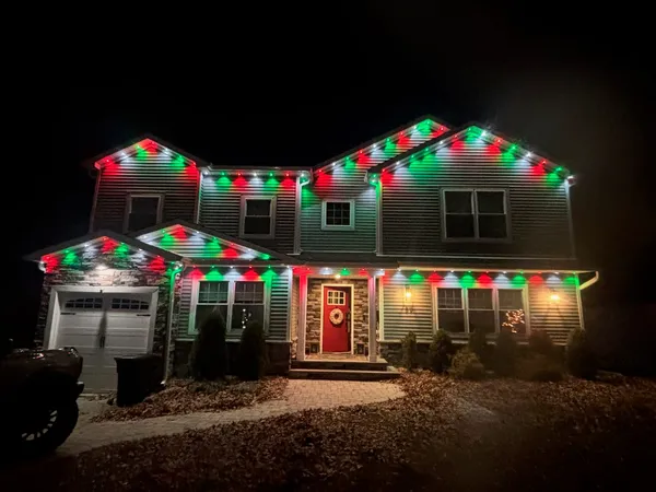 Two-story home at night with red, green and white lights on every gable and roofline and a wreath on the red front door